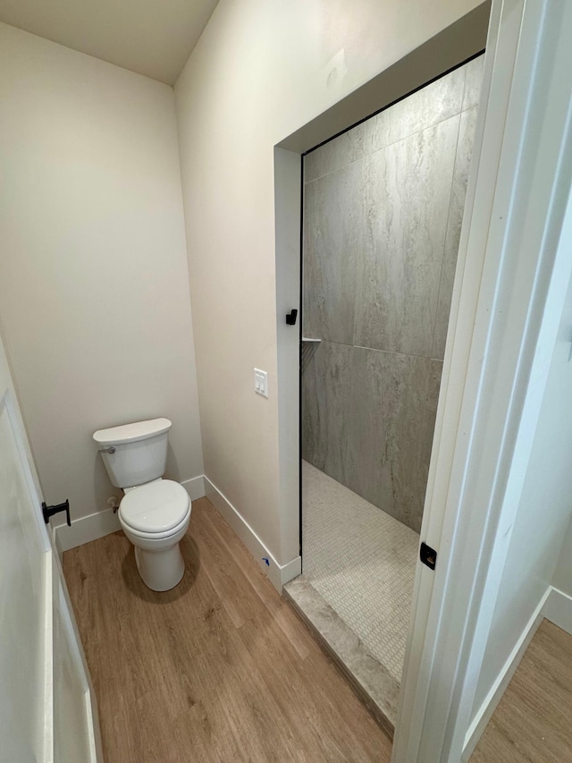 bathroom with baseboards, a walk in shower, toilet, and wood finished floors