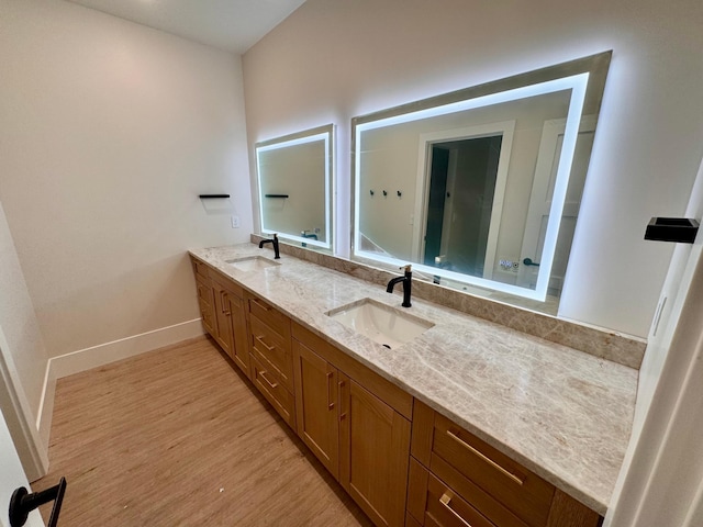 bathroom featuring baseboards, a sink, wood finished floors, and double vanity