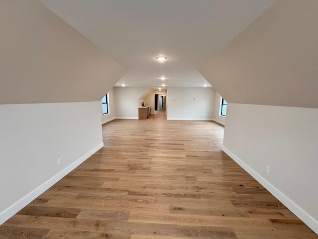 additional living space with baseboards, vaulted ceiling, and light wood finished floors