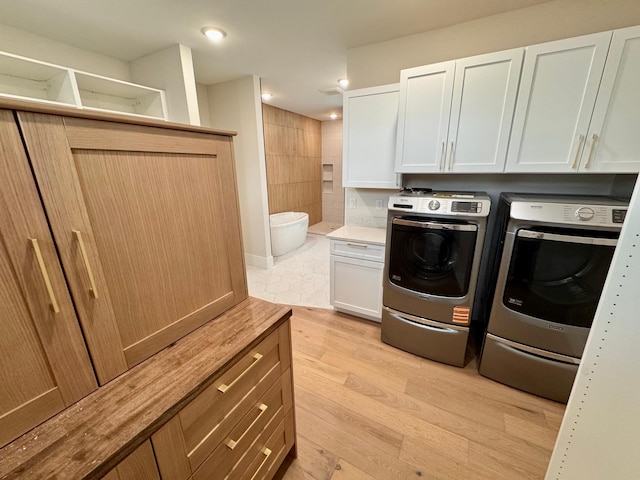 clothes washing area with washing machine and clothes dryer, recessed lighting, light wood-style flooring, and cabinet space
