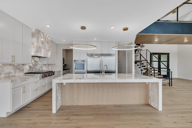 11694 Indian Beach Rd, Spicer, MN 56288 - kitchen featuring appliances with stainless steel finishes, light wood-style flooring, white cabinetry, decorative backsplash, and a large island with sink