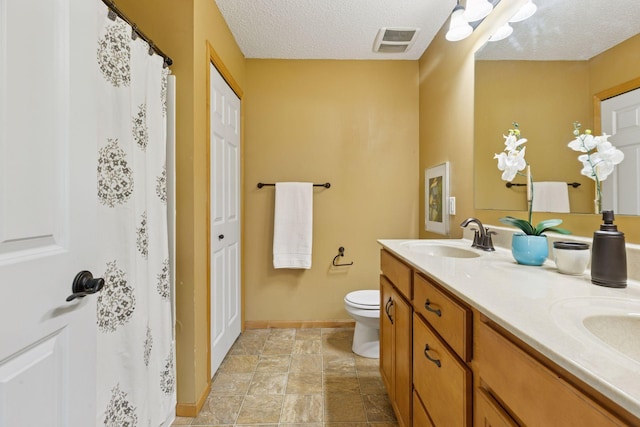 9512 Scott Ln N, Brooklyn Park, MN 55443 - bathroom featuring baseboards, double vanity, toilet, and a textured ceiling