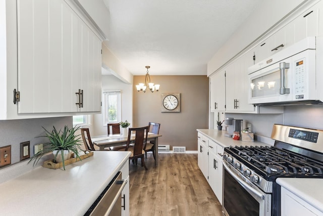 kitchen with white microwave, stainless steel range with gas stovetop, light countertops, a chandelier, and white cabinets