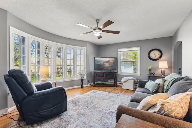 living room featuring a ceiling fan, baseboards, wood finished floors, arched walkways, and a textured ceiling