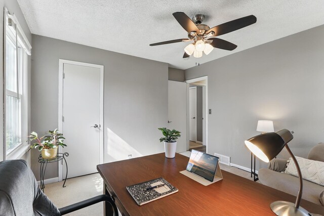 home office with ceiling fan, light carpet, baseboards, and a textured ceiling