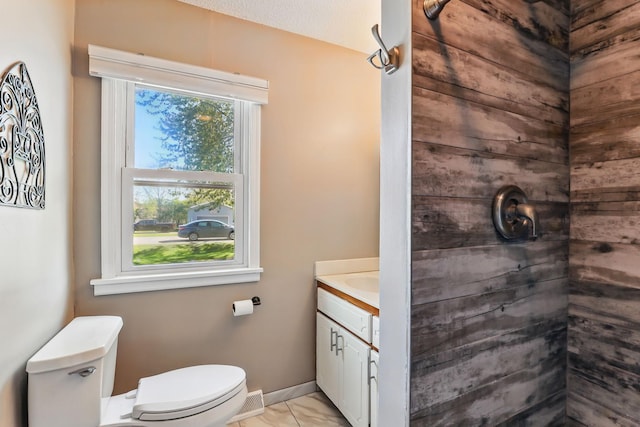 bathroom featuring toilet, vanity, marble look tiles, baseboards, and tiled shower