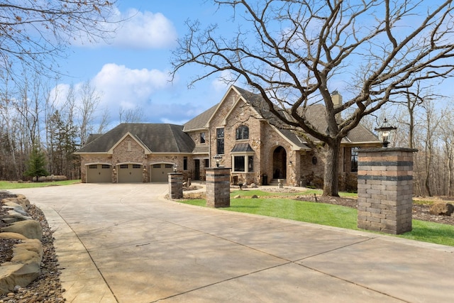 french country inspired facade with a garage, stone siding, roof with shingles, brick siding, and driveway
