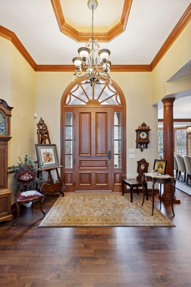foyer entrance with a notable chandelier, a raised ceiling, decorative columns, wood finished floors, and ornamental molding