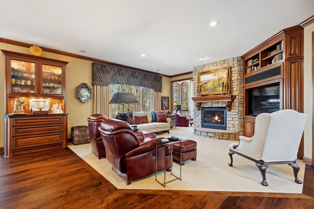 living area with a stone fireplace, ornamental molding, and wood finished floors