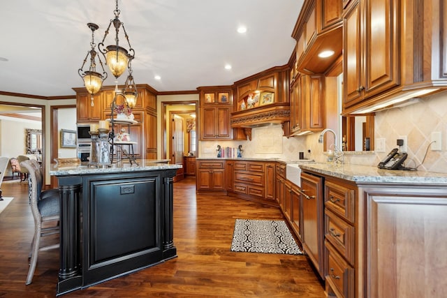kitchen featuring light stone counters, a sink, decorative light fixtures, and ornamental molding