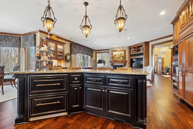 kitchen with a center island, light stone countertops, dark wood finished floors, ornamental molding, and dark cabinetry