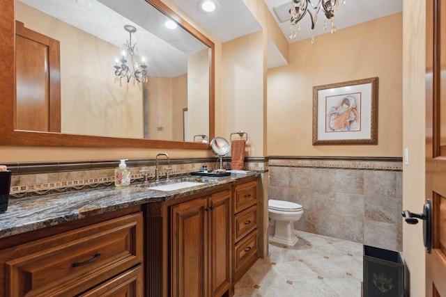 bathroom featuring a notable chandelier, vanity, toilet, a wainscoted wall, and tile walls