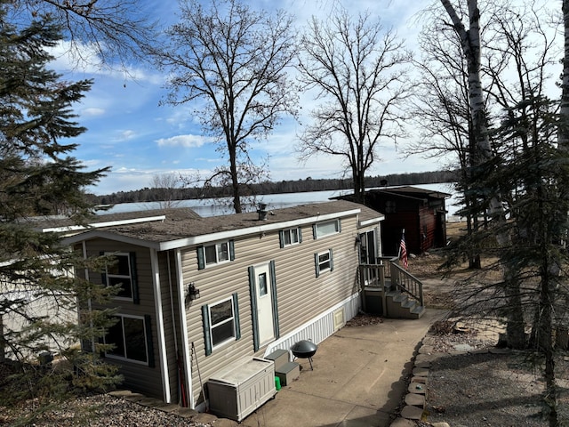 back of property with a water view and a shingled roof