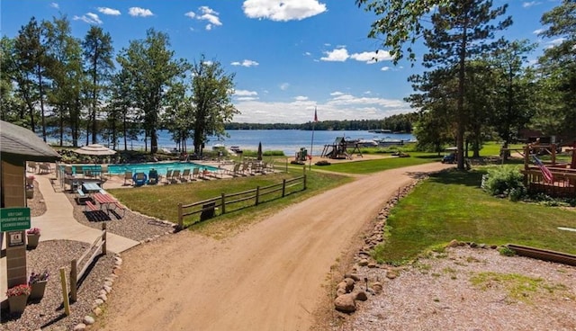 view of property's community featuring a pool, a water view, a yard, and dirt driveway