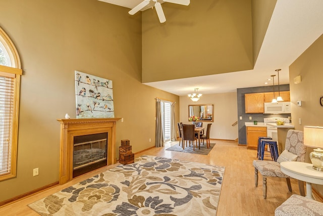 living area with a high ceiling, ceiling fan with notable chandelier, baseboards, and light wood-type flooring