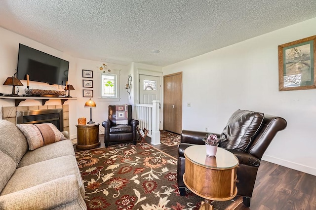 living area featuring baseboards, a textured ceiling, a glass covered fireplace, and wood finished floors