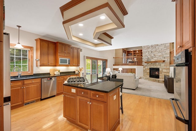 6507 Orchard Ridge Trl, Woodbury, MN 55129 - kitchen featuring appliances with stainless steel finishes, light wood-style flooring, a fireplace, a kitchen island, and a breakfast bar
