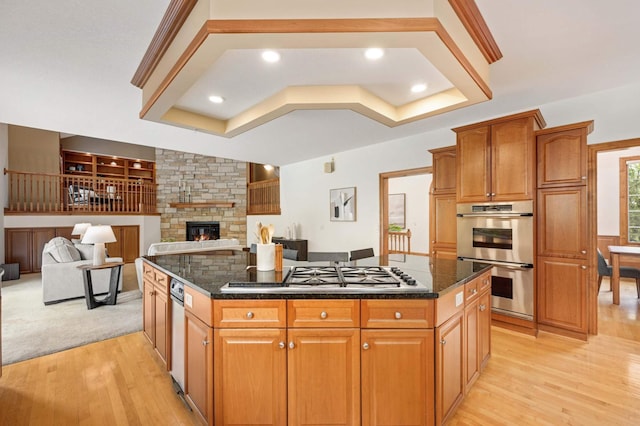 6507 Orchard Ridge Trl, Woodbury, MN 55129 - kitchen with stainless steel appliances, light wood-style floors, a fireplace, dark stone countertops, and a kitchen island