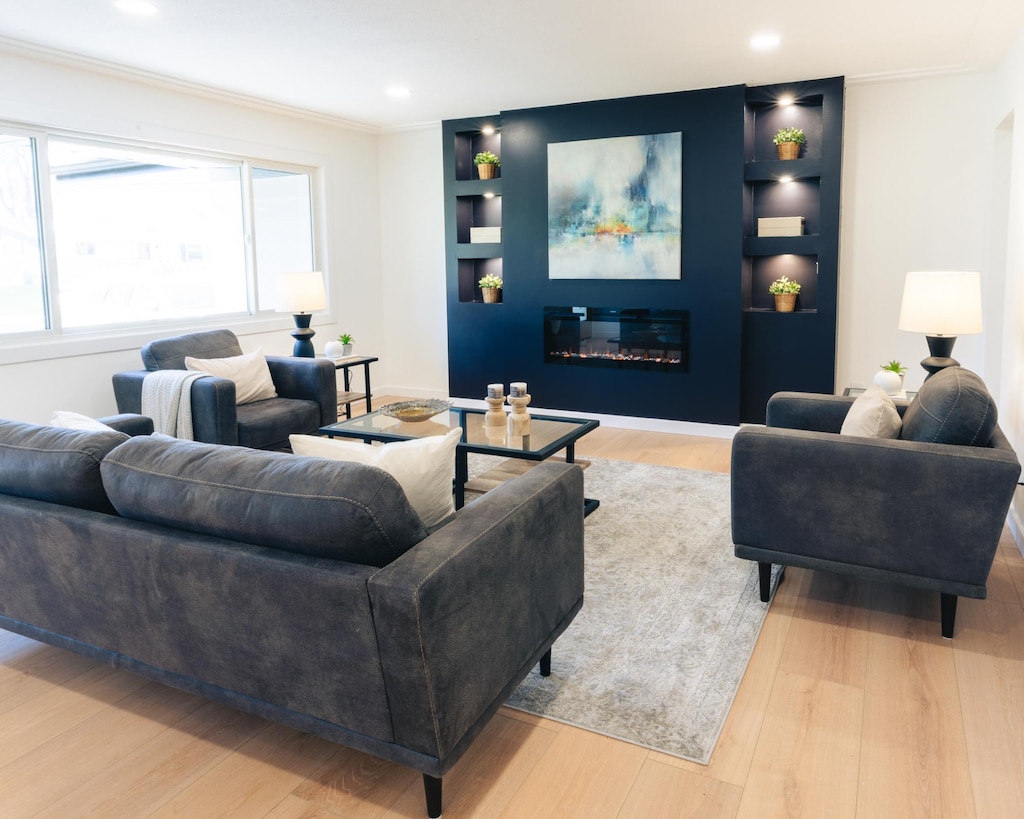 living area with ornamental molding, built in features, a glass covered fireplace, wood finished floors, and recessed lighting