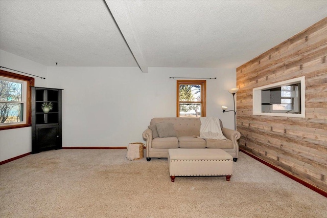 carpeted living room featuring wood walls, a textured ceiling, baseboards, and beam ceiling