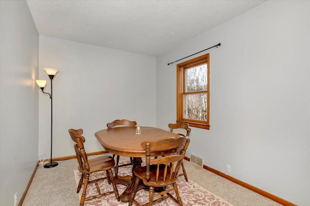 dining space with light colored carpet, baseboards, and a textured ceiling