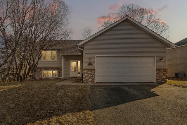 view of front of home featuring aphalt driveway, brick siding, a garage, and central AC