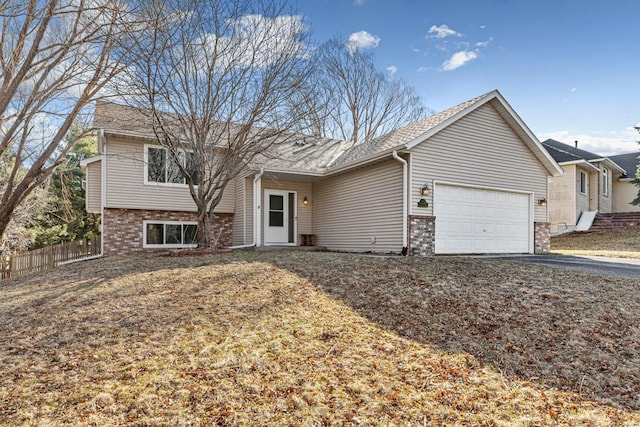 tri-level home with aphalt driveway, a garage, fence, and brick siding