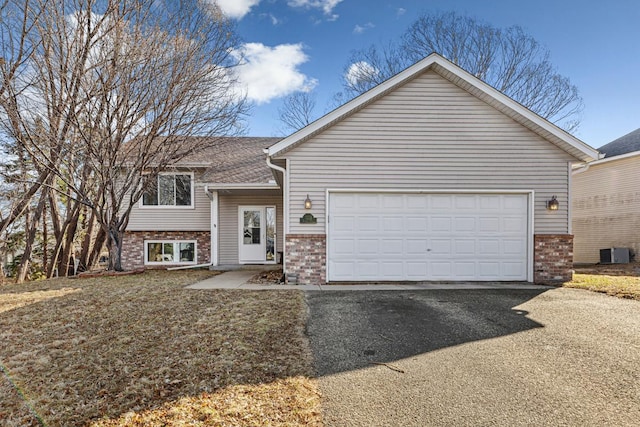view of front facade featuring central air condition unit, a garage, brick siding, and aphalt driveway