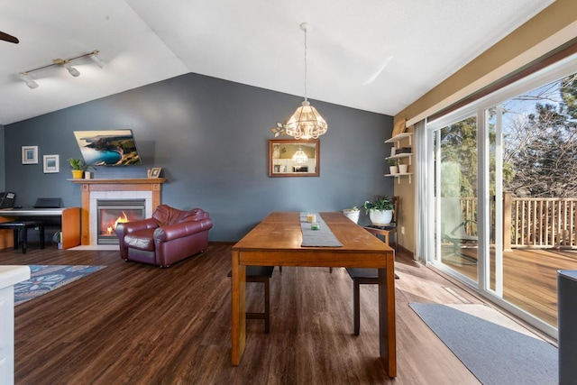 dining space featuring lofted ceiling, a tiled fireplace, wood finished floors, and a chandelier