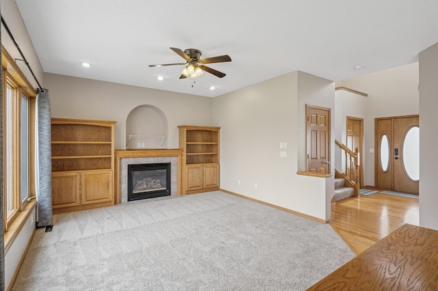 unfurnished living room with light wood finished floors, a premium fireplace, ceiling fan, stairs, and baseboards