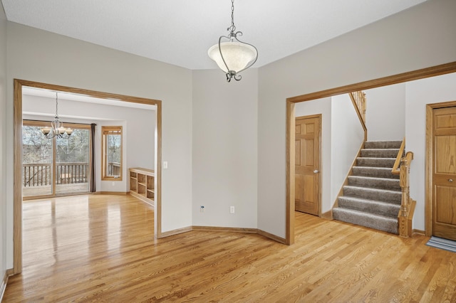 empty room featuring stairs, light wood-style flooring, a chandelier, and baseboards