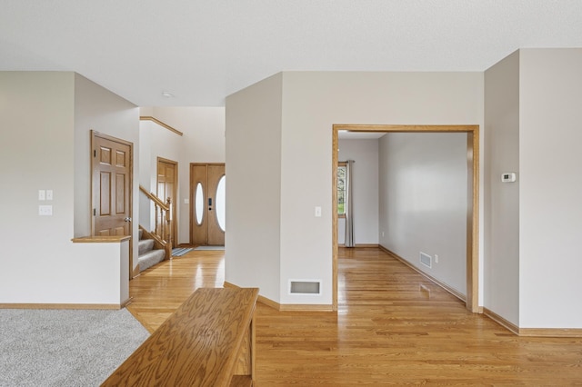 empty room featuring baseboards, visible vents, stairway, and light wood-type flooring