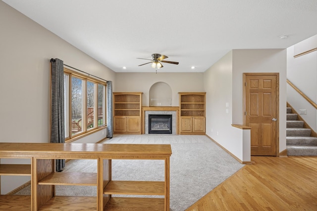 unfurnished living room with light wood finished floors, a tile fireplace, ceiling fan, stairs, and baseboards