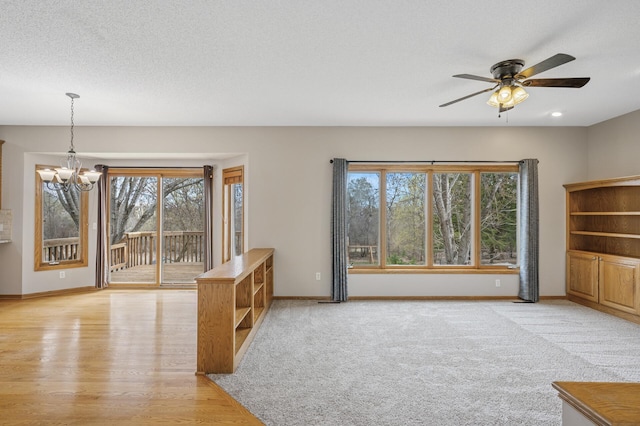 unfurnished living room featuring baseboards, ceiling fan with notable chandelier, and light wood-style floors