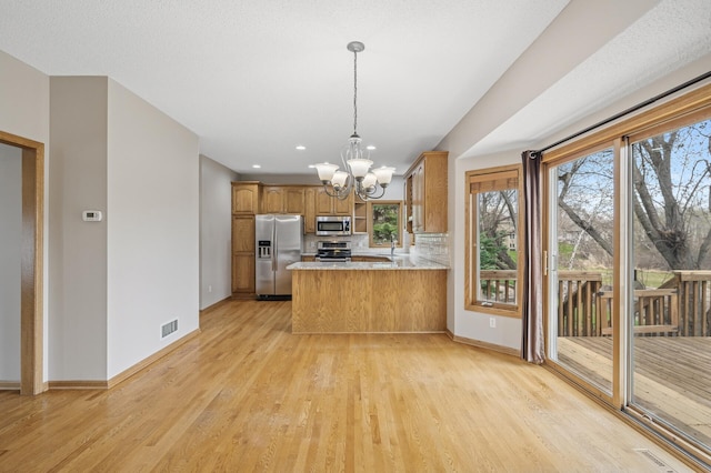 kitchen with appliances with stainless steel finishes, brown cabinets, light wood finished floors, visible vents, and a notable chandelier