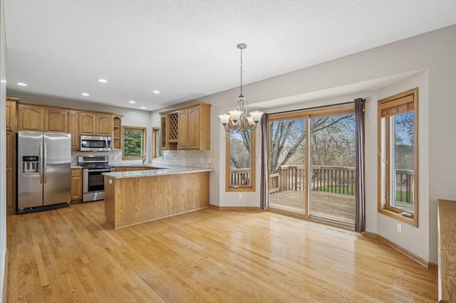 kitchen featuring decorative backsplash, stainless steel appliances, light wood-style floors, a notable chandelier, and a peninsula