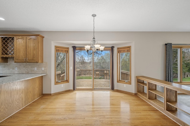 unfurnished dining area featuring a healthy amount of sunlight, baseboards, a notable chandelier, and light wood-style flooring