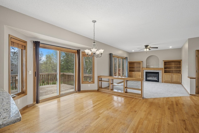 interior space featuring recessed lighting, a glass covered fireplace, light wood-style flooring, baseboards, and ceiling fan with notable chandelier