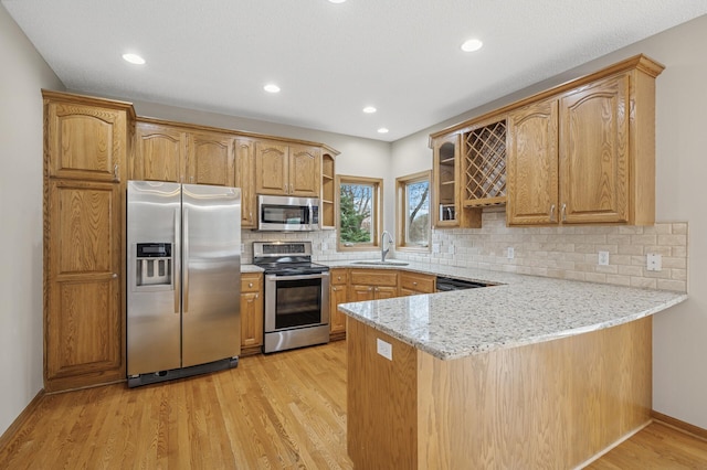 kitchen featuring light wood-style flooring, stainless steel appliances, open shelves, a sink, and a peninsula