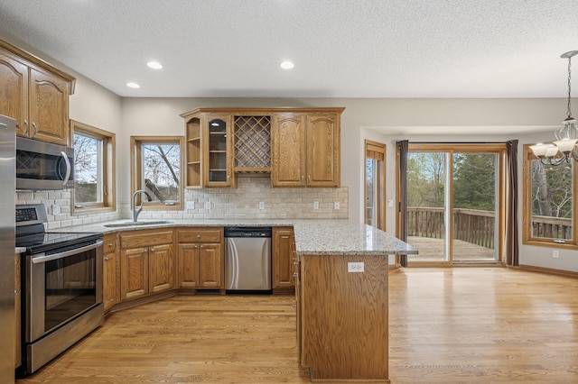 kitchen with appliances with stainless steel finishes, brown cabinets, a sink, light wood-type flooring, and a peninsula