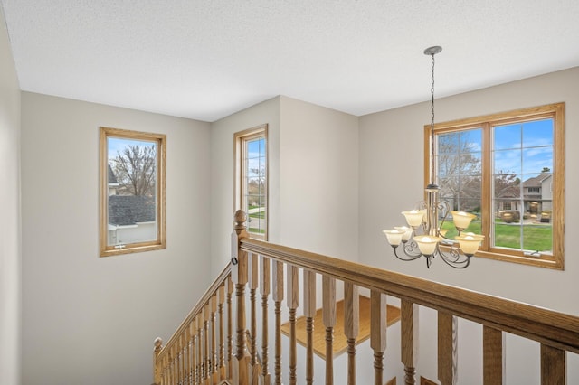 corridor featuring an upstairs landing and a notable chandelier