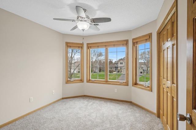 unfurnished room featuring baseboards, light carpet, a textured ceiling, and ceiling fan