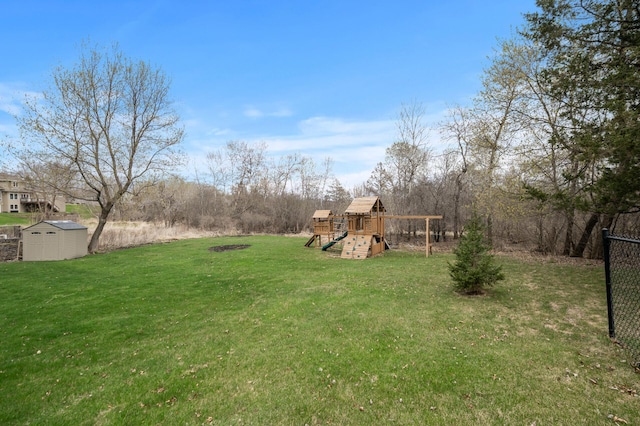 view of yard with fence, a storage unit, an outbuilding, and a playground