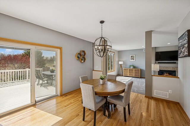 dining room featuring an inviting chandelier, a glass covered fireplace, visible vents, and light wood-style flooring