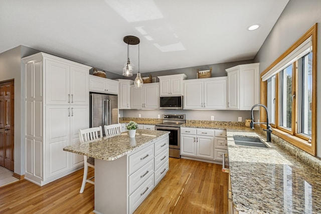 kitchen with white cabinets, stainless steel appliances, light wood finished floors, and a sink