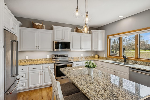 kitchen with a sink, stainless steel appliances, light wood-style floors, a breakfast bar area, and white cabinets