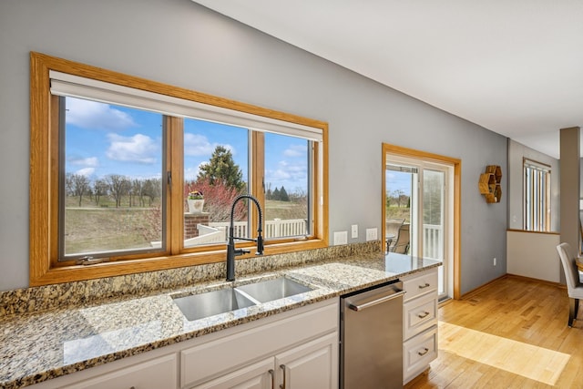 kitchen featuring white cabinetry, a sink, light wood-type flooring, light stone countertops, and dishwasher