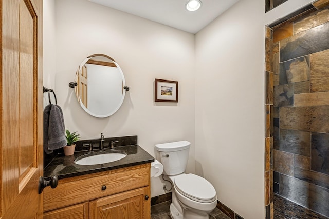 bathroom featuring baseboards, a tile shower, toilet, and vanity