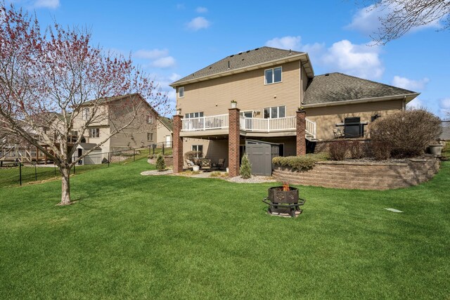back of property with a fire pit, fence, a shingled roof, a wooden deck, and a lawn