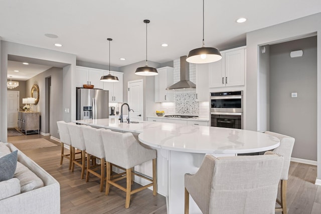 19477 102nd Pl, Corcoran, MN 55374 - kitchen featuring wall chimney range hood, appliances with stainless steel finishes, backsplash, white cabinets, and light wood-type flooring